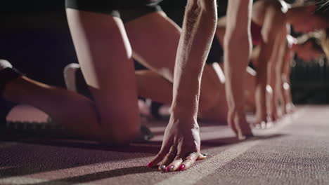 Vista-Lateral-De-Tres-Mujeres-Preparándose-Para-Correr-En-El-Estadio-En-La-Oscuridad-En-Cámara-Lenta-Comenzando-Y-Corriendo-Hacia-La-Cámara